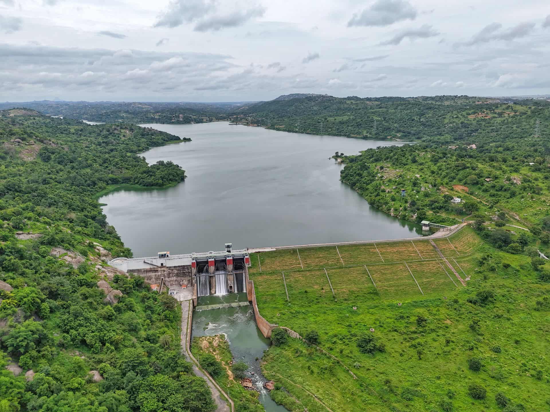 A dam holding back a reservoir, with wooded green hills rolling away beyond the water