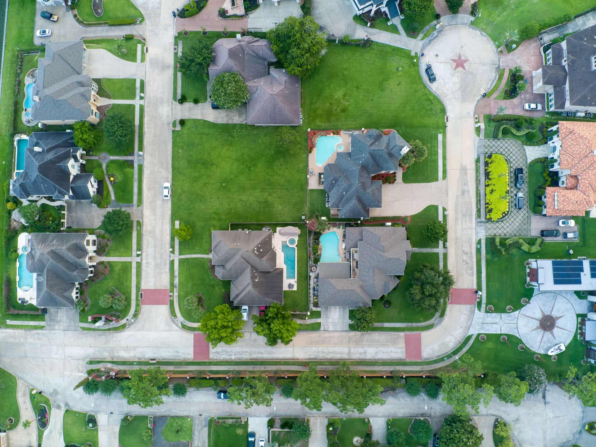 Aerial view of a residential street of large homes on wide, tree-shaded lots with backyard pools