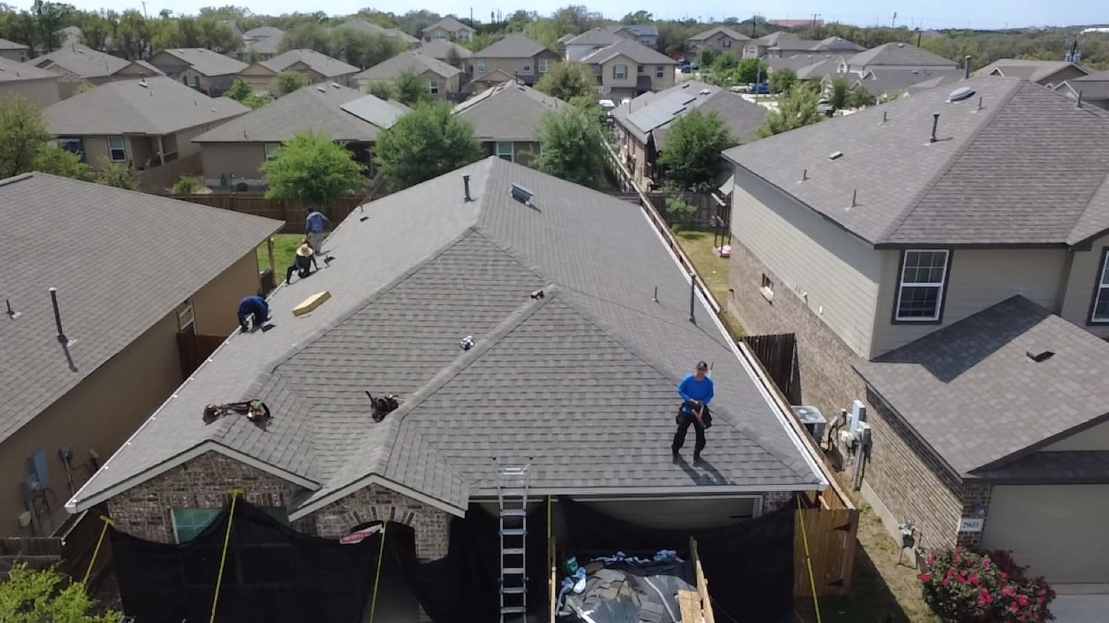 Inspector on the roof of a San Antonio home checking shingles, ladder set at the eave