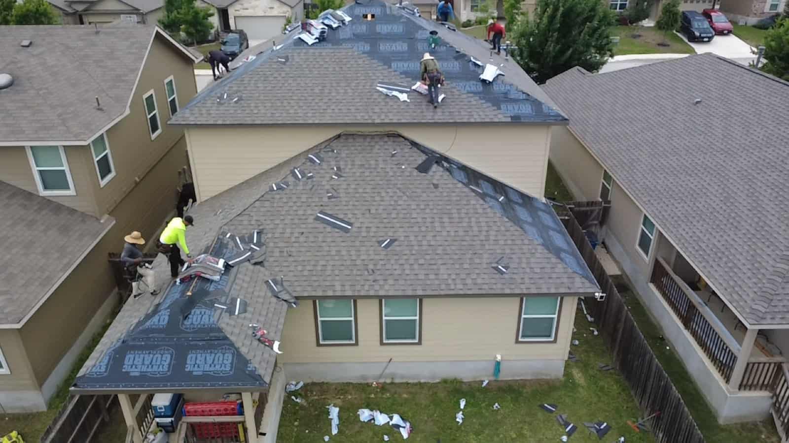 Roofing crew installing synthetic underlayment during a full roof replacement, seen from above