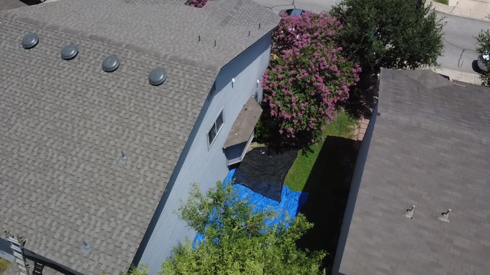 Aerial view of a San Antonio shingle roof with ridge vents and an emergency tarp staged in the yard after a leak