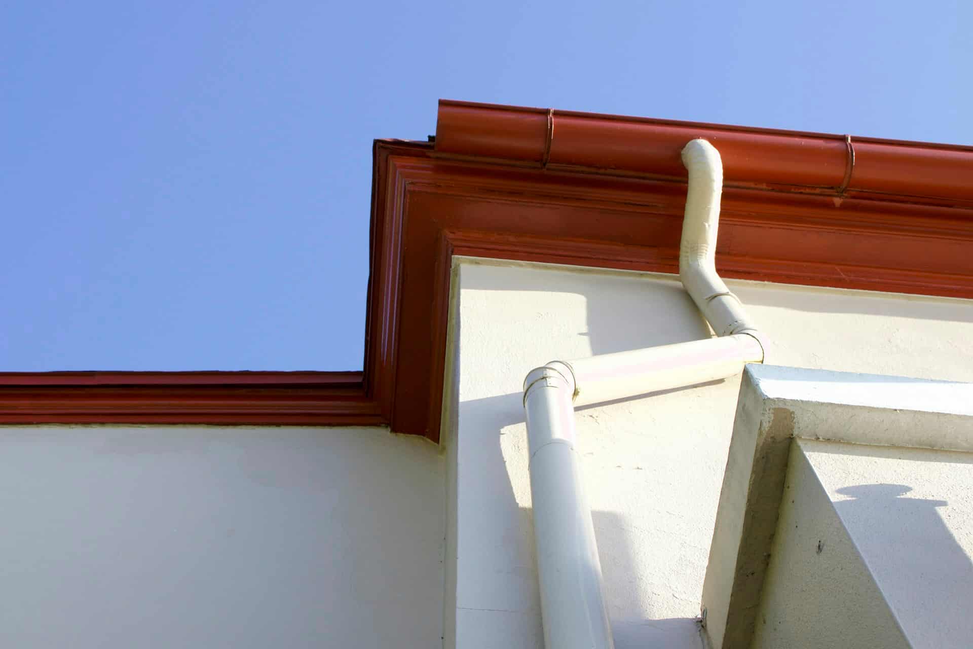 Seamless rain gutter and downspout mounted at the corner of a stucco home