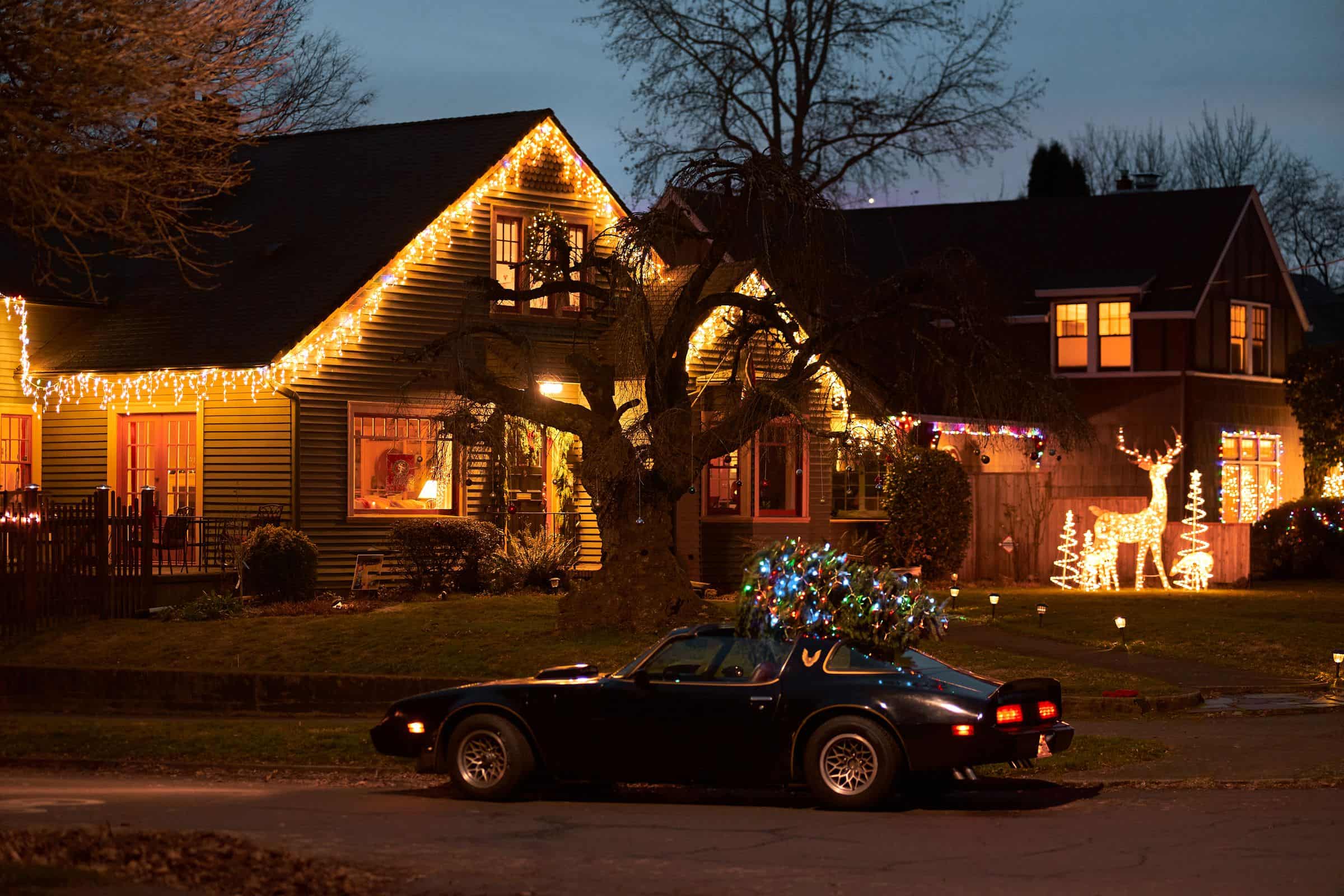 Suburban home at dusk with warm white Christmas lights outlining the rooflines and gables, neighbouring houses lit down the street