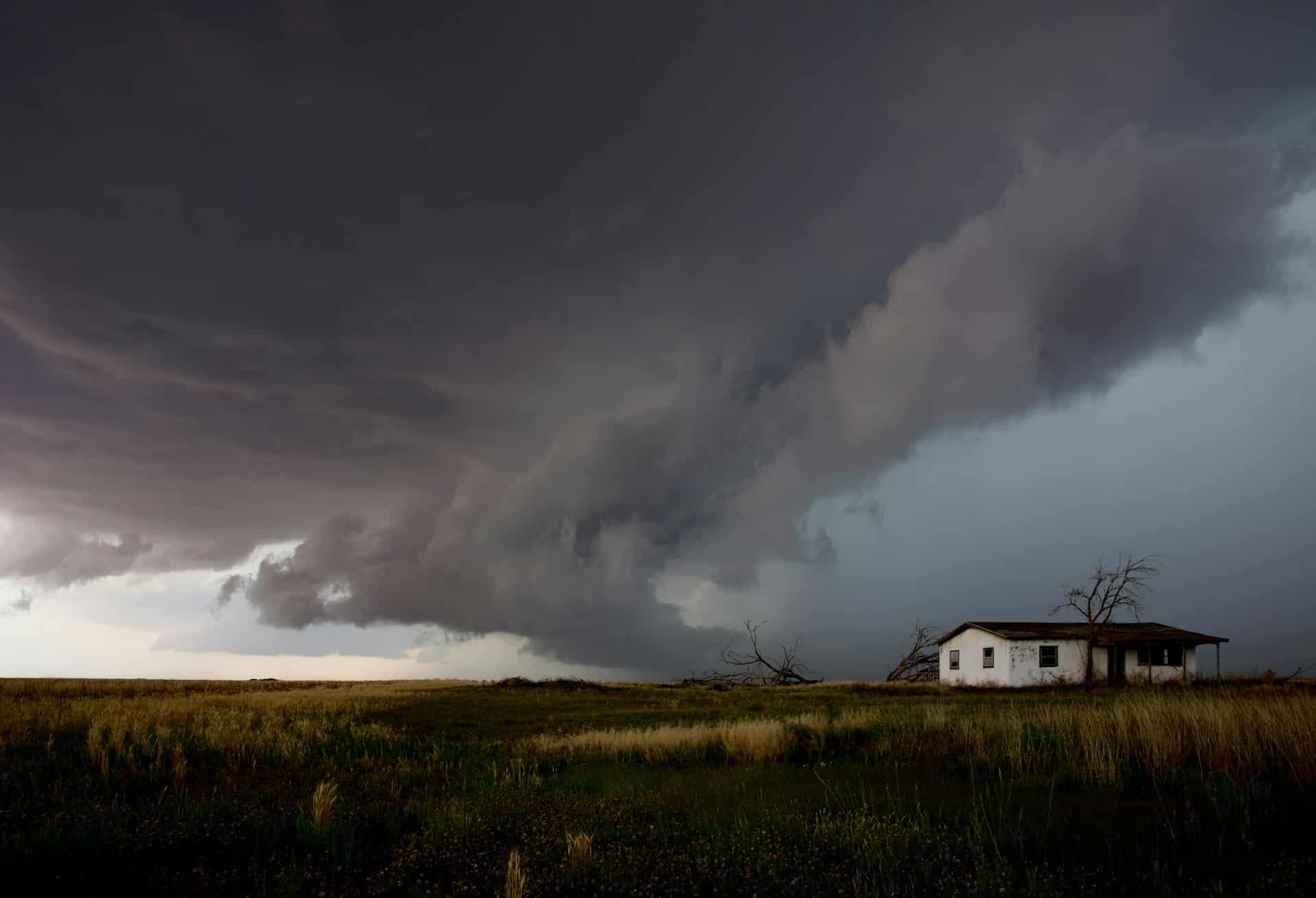Dark supercell storm cloud rolling over a small Texas prairie farmhouse